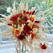 Full-size bohemian preserved bridal bouquet featuring fiery red and burnt orange roses, pampas grass, craspedia, and wild dried textures