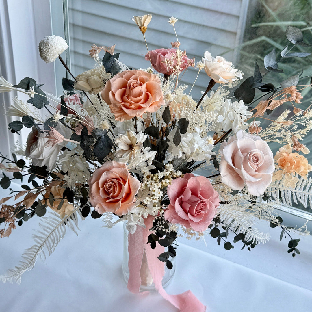Coral blush handcrafted preserved bridal bouquet with garden roses, hydrangeas, and dark foliage, arranged in a romantic organic shape