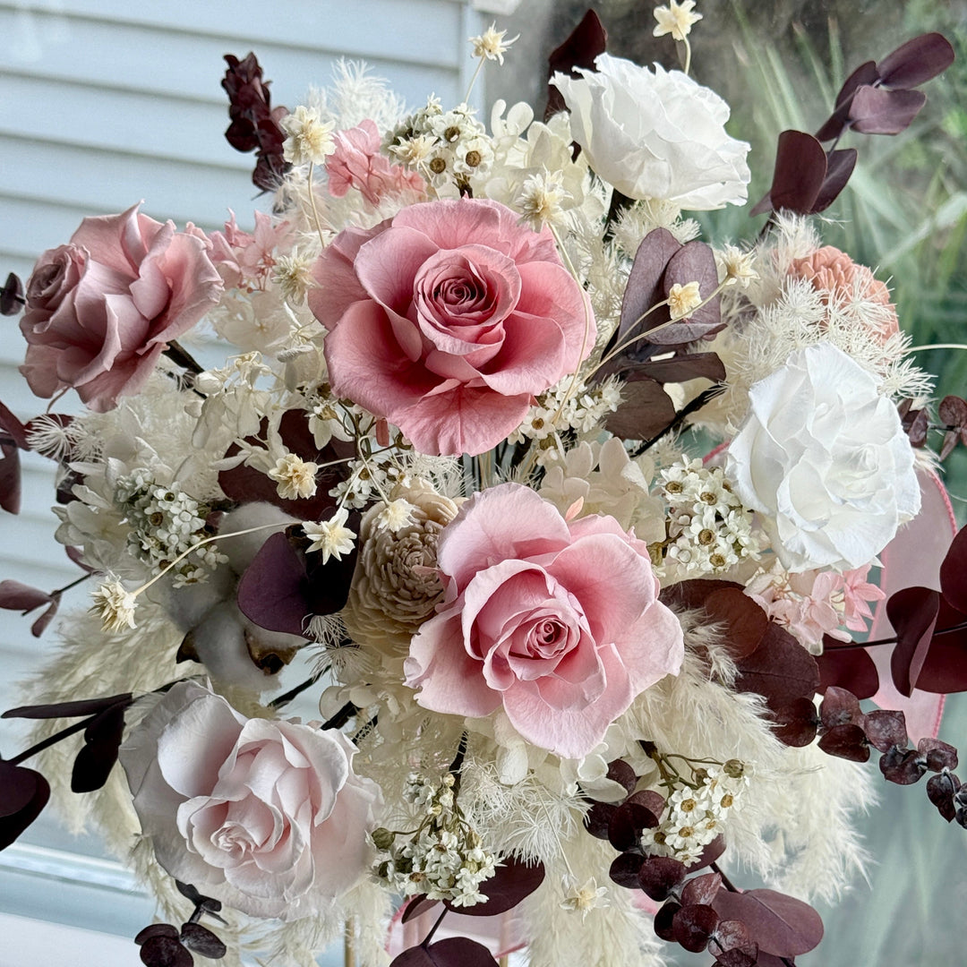 Close-up of blush pink preserved roses surrounded by ivory florals and textured foliage